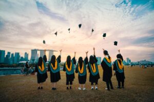 Group of fresh graduates celebrating by throwing their caps into the air at sunset